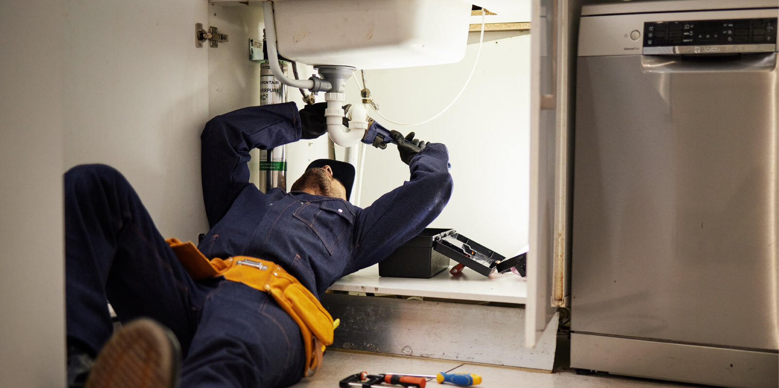 Plumber underneath a sink working on repairing a broken pipe.